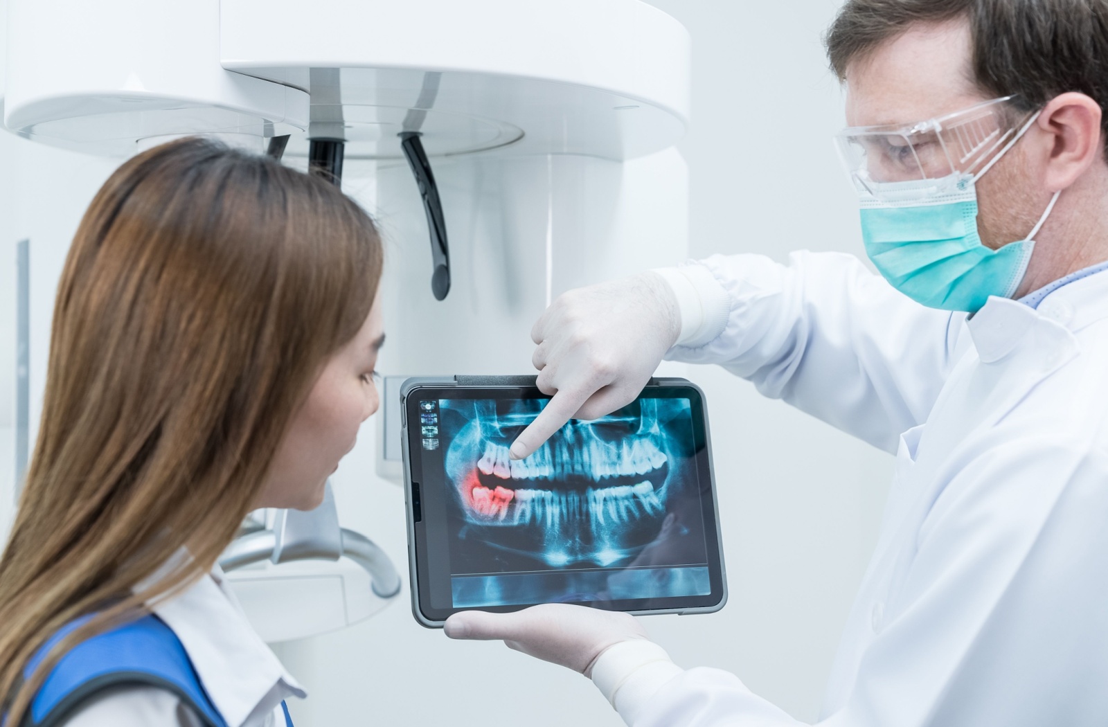 A dentist utilizes a tablet to show a young patient the problem area of their mouth that needs restorative work