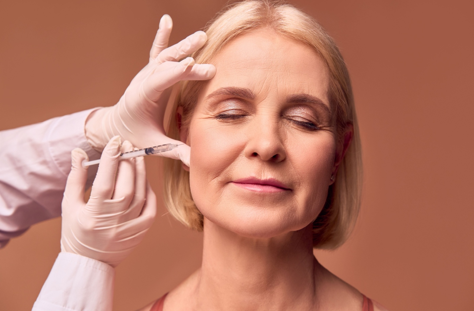 A mature adult sits in a clinic and receives Botox injections into their forehead.