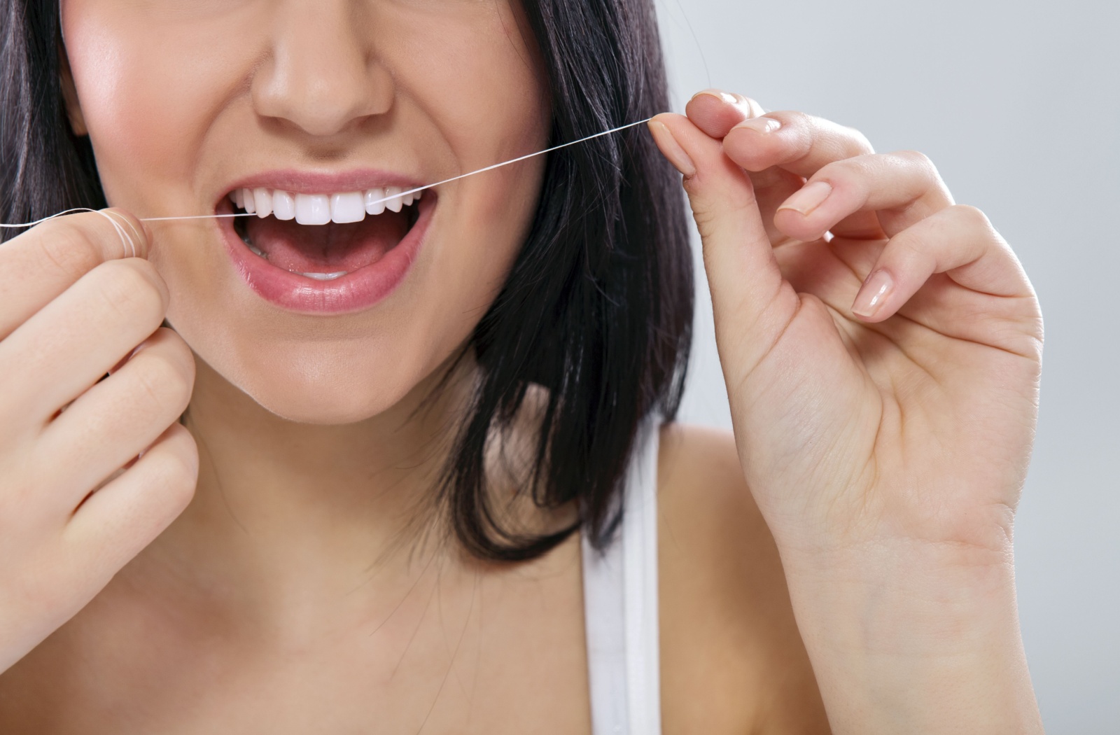 Close-up of a person's mouth as they run floss between their front teeth.