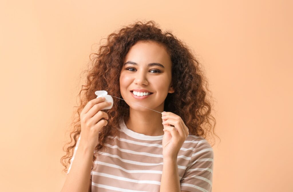 A person flossing their teeth standing in front of an orange background.