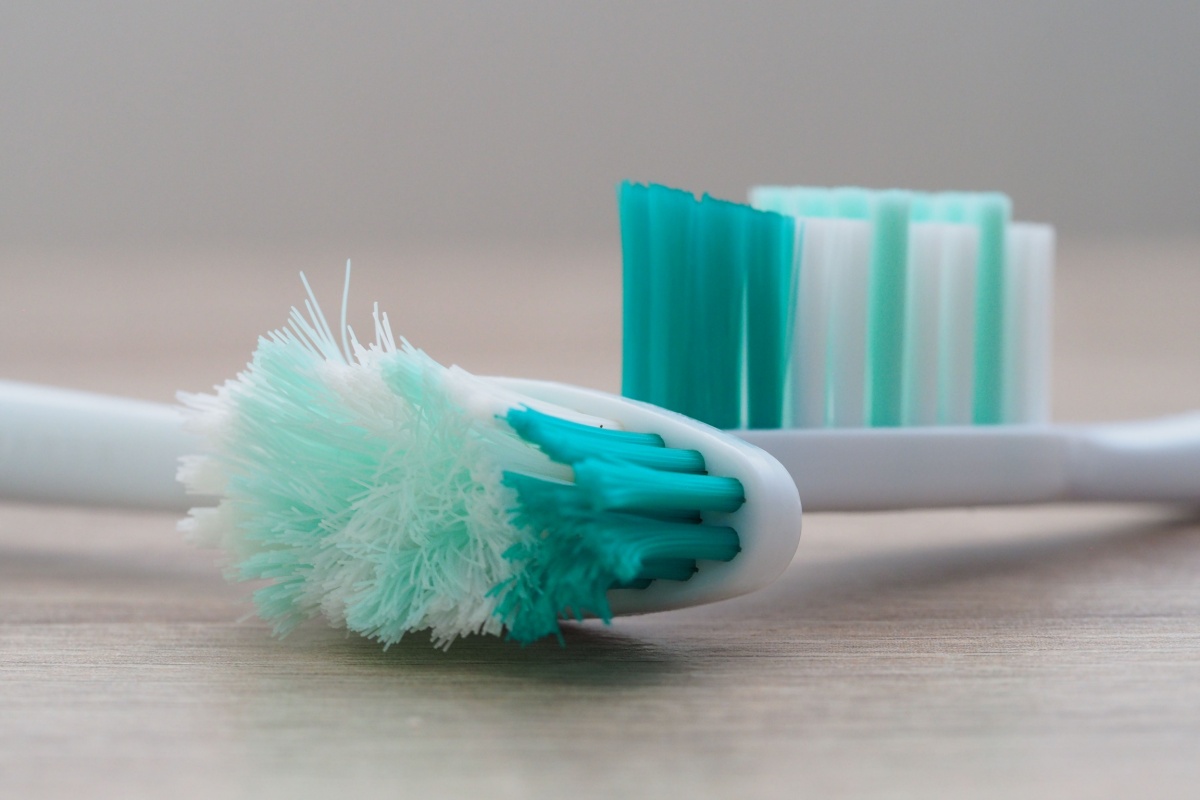 Close-up view of a worn-out manual toothbrush with frayed, splayed bristles lying on a flat surface.